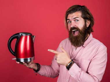 Şuna bir bak. Oda servisinde kullanışlı. Olgun karizmatik erkek elektrikli su ısıtıcısı kullanır. Sakallı ve bıyıklı adam çay yapıyor. Sıcak çay iç. Sakallı adam mağaza asistanı mutfak aletlerini sunar.