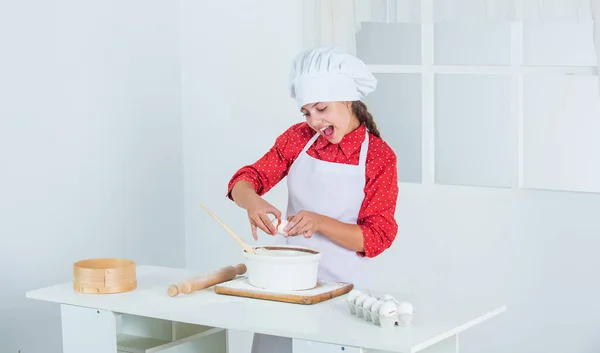 Diligent approach. happy child cooking in kitchen. bake cookies in kitchen. professional and skilled baker. kid in chef uniform and hat. teen girl preparing dough. making cake by recipe. time to eat — Stock Photo, Image