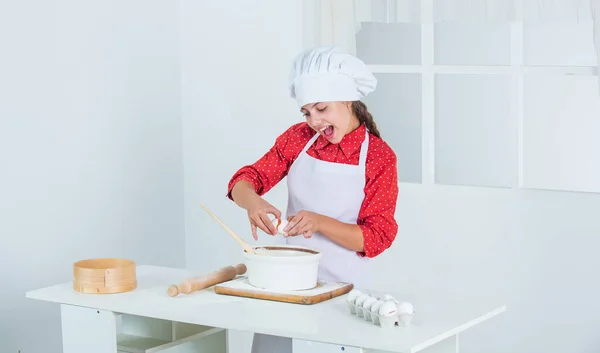 Enfoque diligente. feliz niño cocinando en la cocina. hornear galletas en la cocina. panadero profesional y experto. niño con uniforme de chef y sombrero. adolescente chica preparando la masa. hacer pastel por receta. hora de comer — Foto de Stock