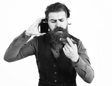 Sakallı adam puro içiyor, ciddi bir yüzü var, parfüm tutuyor.