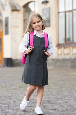 Resmi üniformalı küçük çocuk okula çantasıyla gider, okula geri döner.
