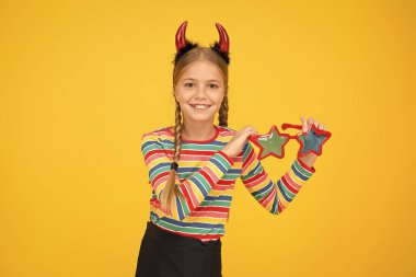 Cadılar Bayramı bu aksesuarla dolu olsun. Küçük çocuk sarı arka planda Cadılar Bayramı aksesuarı giyiyor. Küçük kız moda göz aksesuarı tutuyor. Cadılar Bayramı için parti aksesuarı