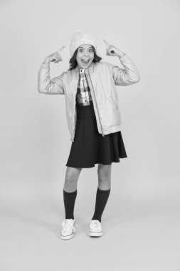 Çılgınca. Mutlu çocuk sarı arka planı. Soğuk mevsim için sıcak kıyafetler. Moda kızı hipster 'a benziyor. Küçük kız kış şapkası. Modayı takip eden liseli kızlar ceket ve uzun çoraplar giyer. Kıyafet dükkanı.