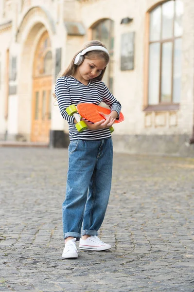 Bambino piccolo tenere penny board e ascoltare musica in cuffie all'aperto, skateboard — Foto Stock