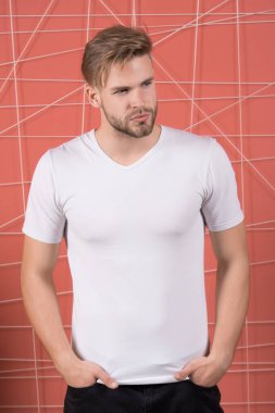 Avrupalı genç bir adam elleri ceplerinde duruyor. Pembe arka planda fotokopi alanı için beyaz tişört giyiyor.