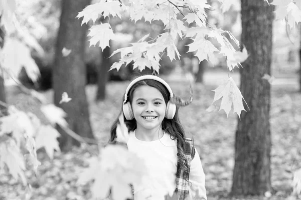 Roztomilý dětský úsměv se stereo sluchátky. Podzimní melodie. Školačka poslouchá moderní sluchátka. Technologie sluchátek. Padající listí. Šťastná holčička nosit sluchátka podzimní příroda pozadí — Stock fotografie