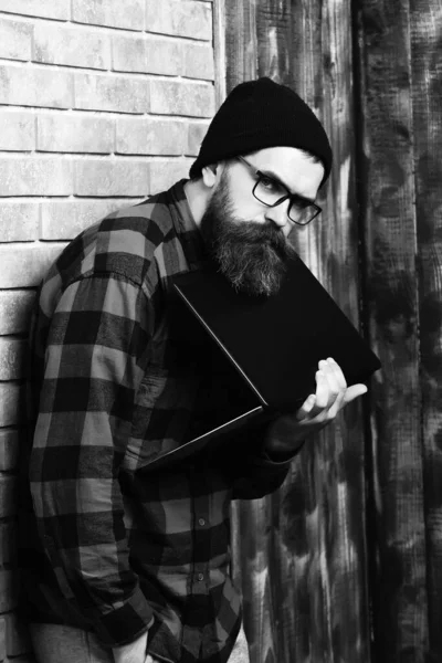 Barbudo brutal caucasiano hipster segurando laptop no bege tijolo parede estúdio fundo — Fotografia de Stock