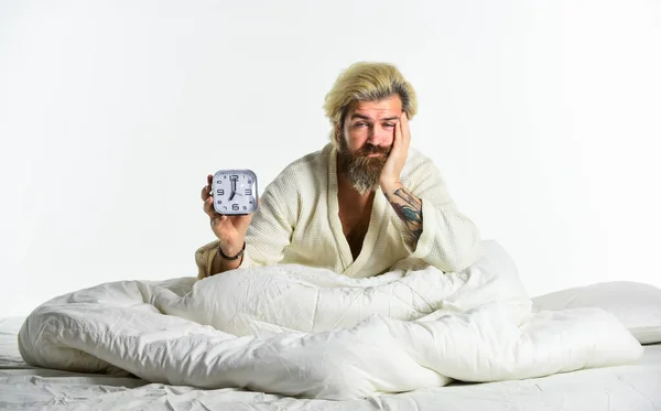 Bearded man with alarm clock. Awakening. Sleep complex biological process that helps process new information, stay healthy and feel rested. Stressed man alarm clock. Sleepy guy and alarm clock in bed