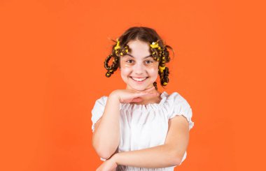 Moda ipuçları. Gençlik hobileri. Kıvırcık saçlı, turuncu saçlı küçük bir kız. Kafasında bigudileri olan kızı gülüyor. Kuaför salonu. Sevimli çocuk saçı. Kadın güzellik rutini