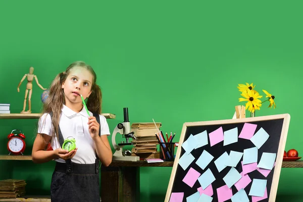 Menina segura lápis verde e relógio. Material escolar e infantil — Fotografia de Stock