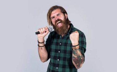 Sanat. Mikrofonda şarkı söyleyen sakallı adam. Sahnede özgüven ve karizma. Kareli gömlek giyen sakallı bir adam. Rock müzik. Erkek karaoke şarkıcısı. Olgun karizmatik erkek vokalist