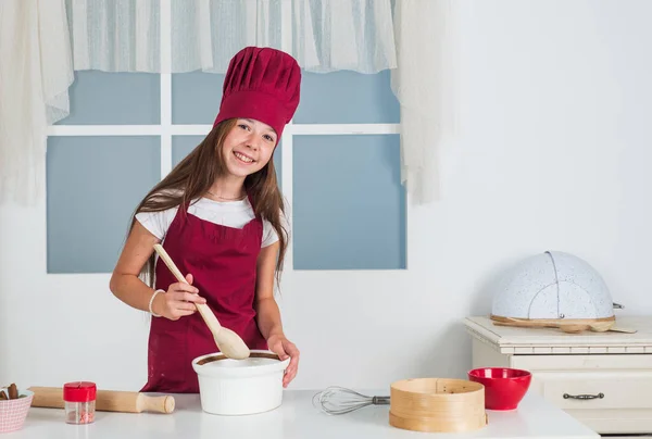 맛있는 식사를 하 세요. 아동 발달. 부엌에서 굽는 작은 소녀. 나무 숟가락으로 요리하는 꼬마 요리사. 아이들은 집에서 건강에 좋은 음식을 준비하고 요리용 유니폼을 입습니다. 집안일과 집안일돕기 — 스톡 사진