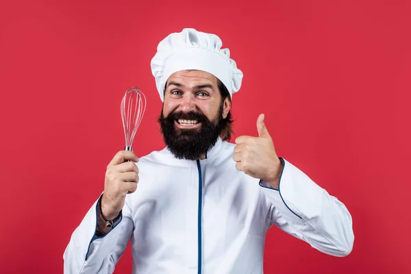 Geschoolde bakker gebruik keukengerei voor het koken. mannelijke chef-kok in hoed bereiden gezonde maaltijd. Knappe man met baard en snor die eten kookt. professioneel restaurant koken bakken. goede kwaliteit van de klopper — Stockfoto