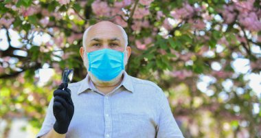 Yetenekli doktor. Solunum maskesi ve eldiven giymiş yaşlı bir adam. Parkta sakura çiçeği ağacı. Koronavirüs kovid 19. Bahar keyfi. Yasak Sakura Parkı. Park koronavirüs nedeniyle karantinaya alınmıştır.
