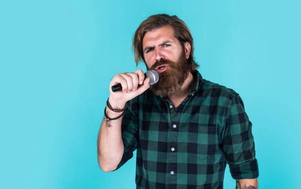 Guy with beard singing in microphone. confidence and charisma on stage. bearded man wearing checkered shirt. rock music. male karaoke singer. mature charismatic male vocalist. copy space — Stock Photo, Image