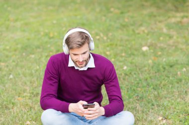 Parktaki genç çekici adam akıllı telefonda şarkı ve şarkı değiştirirken aynı zamanda kablosuz kulaklıkla müzik dinliyor.
