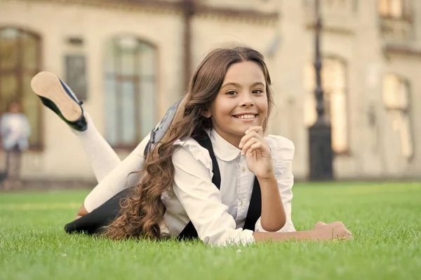 Férias escolares para descansar. Feliz aluno sorridente. Menina bonito garoto que coloca grama verde. Miúdo feliz a relaxar ao ar livre. Uniforme da escola menina desfrutar relaxar. Aluna alegre. Relaxe no pátio da escola. Boa hora. — Fotografia de Stock