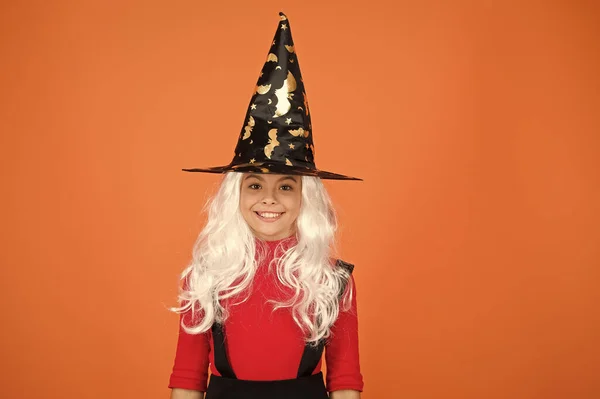 In holiday mood. magic fantasy. smiling girl halloween party. mystery witch. small child witch hat. trick or treat. supernatural charmer gray hair. kid enchantress orange background. happy halloween — Stock Photo, Image
