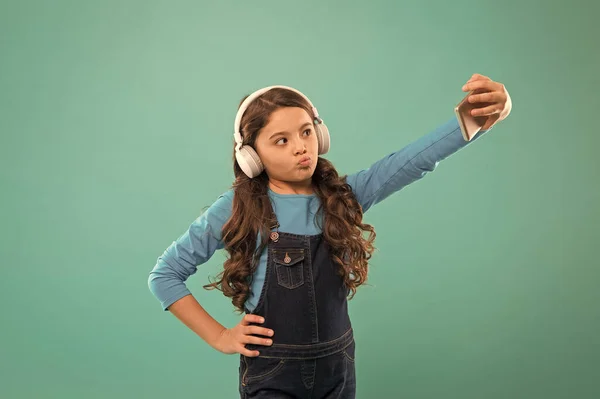 Pozowanie do zdjęcia. Selfie dzieciak w słuchawkach. mała rozmowa wideo dziecka na smartfonie. Mała dziewczynka trzyma telefon komórkowy. blogowanie we współczesnym życiu. Uczennica używa nowej technologii. żyć w wirtualnym świecie — Zdjęcie stockowe