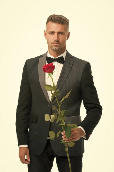 tuxedo man with rose flower. happy valentine day. special occasion. male formal style of clothing. elegant man in suit and tie sexy man on romantic date. Black tie dress code for evening events