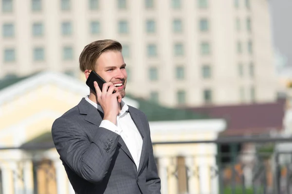 Comunicación empresarial y nuevas tecnologías. Feliz hombre de negocios con smartphone en terraza soleada. Hombre sonrisa en traje formal con teléfono móvil al aire libre. Concepto de estilo de vida — Foto de Stock