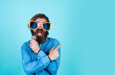 Şuraya bak. Partide iyi eğlenceler. Erkek şarkıcı mikrofonda şarkı söylüyor. Yıldönümünü kutlamak. Partiye katılan. Sakallı hippi gözlüklü adam. Müzik konsepti. İyi tatiller.