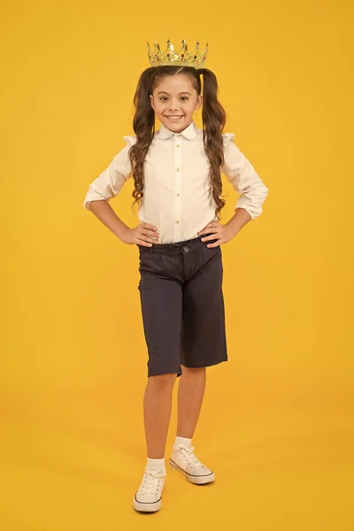 El éxito asiste al trabajo duro. Chica feliz disfrutando del éxito en el fondo amarillo. Pequeño escolar entusiasmado con el éxito. Adorable niño pequeño con corona de éxito —  Fotos de Stock