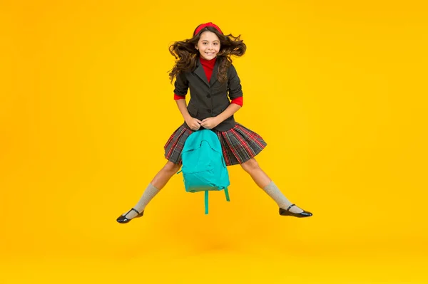 Щаслива маленька дитина в формальній формі тримає шкільну сумку, стрибає в повітрі жовтим фоном, навчаючись — стокове фото