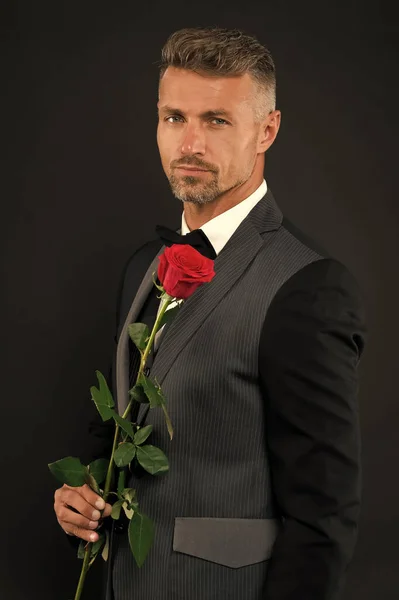 sexy man in black suit hold red rose. magician in tuxedo with red rose. celebrating 14 february. Tuxedo Rose on Wedding Day. nobody looks better. He is wearing formal wear. express attraction