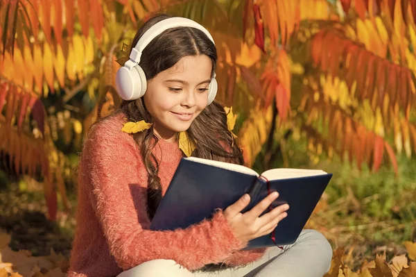 Child enjoy reading. Studying twice faster using visual and audio information. Girl read book on autumn day. Little child enjoy learning in autumn park. Kid study with book. Autumn literature concept