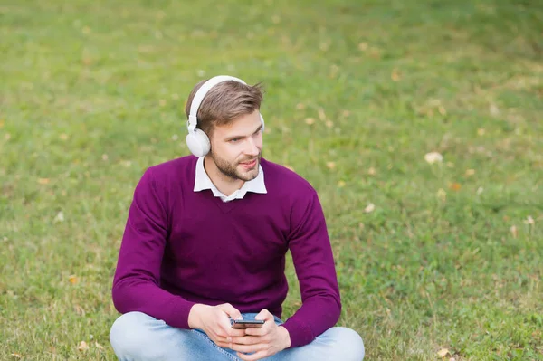 남자는 스마트폰으로 음악을 듣는다. 이어폰을 쓰는 잘생긴 남자는 휴대 전화를 사용 합니다. 현대 생명 기술. mp3 플레이어. 오디오 책으로부터 정보를 얻습니다. 발전하는 개념 — 스톡 사진