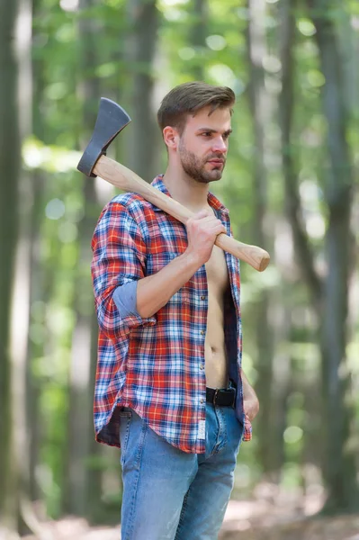 Sexy homem com muscular torso no aberto xadrez camisa com jeans realizar grande divisão machado no verão madeira natural paisagem, natureza — Fotografia de Stock