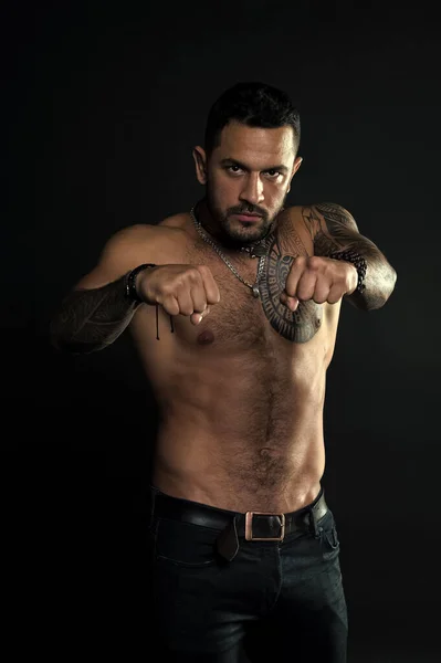 Lets fight. Bearded man with strong torso. Man muscular tattooed arm and chest. Tattoo model sexy belly. Sportsman athlete wear fashionable jeans. Look at my fists. Punch you in face. Muscular man