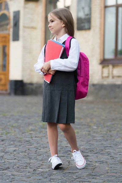 Petit enfant en uniforme formel avec retour à l'école regarder transporter sac tenant des livres et des fournitures, collège — Photo