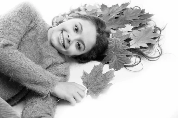 Kinder genießen die Herbstzeit. Mädchen niedliches Kind langes Haar lag auf weißem Hintergrund mit abgefallenen Blättern. Trockene Ahornblätter in Frisur. Herbstzeitkonzept. Haarpflege im Herbst. Trockene Haarspitzen verhindern — Stockfoto