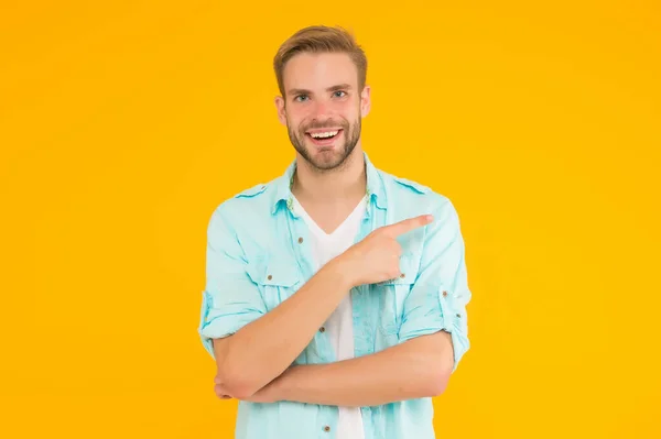 밝은 행복 한 남자가 노란 배경에서 데님 스타일의 옷을 손가락 질하고 입고 제품을 제시하는 모습 — 스톡 사진