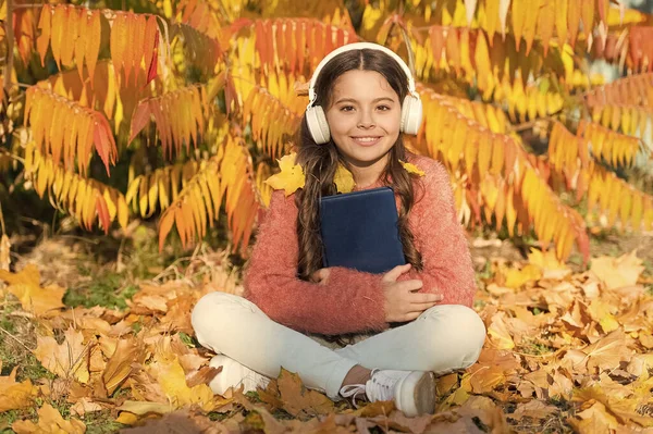 Music is universal language. Happy small child listen to audio language course. Little girl with audio book learn English language on autumn day. Learn to speak foreign language online