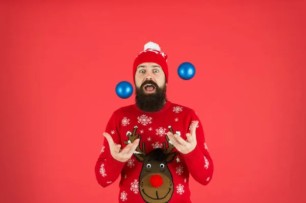 Яйцеподібні кульки. Концепція Нового року. Різдвяна вечірка. Зимове вбрання. Зимові прикраси. Веселі святкові заходи. Хіпстер веселий бородатий чоловік носить зимовий светр і капелюх тримає кульки червоний фон — стокове фото