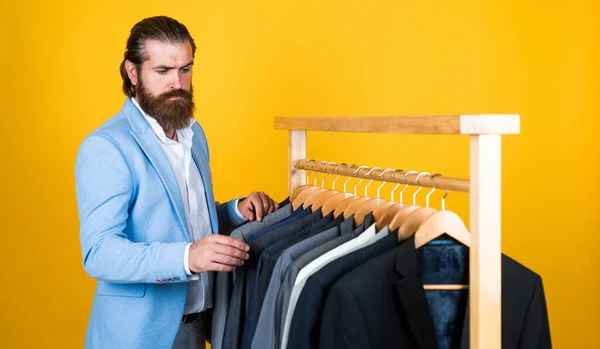 Hip and stylish. business fashion style. dry cleaning service. style and people concept. Handsome man in smart casual wear looking at suits and choosing. stylish mens clothing on hanger stand in room — Stock Photo, Image