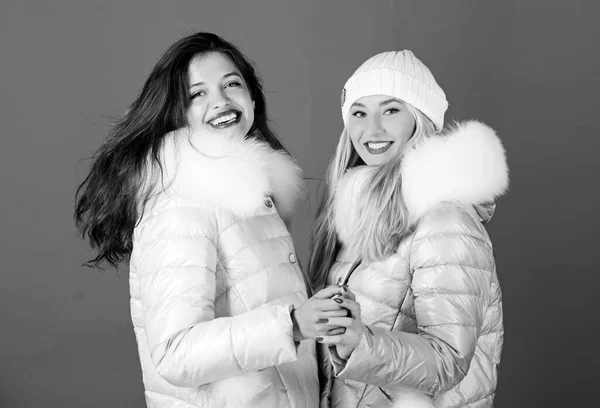 Fashion friends. Winter clothes. Women wear down jacket with furry hood.  Girls smiling makeup faces wear winter jackets blue background. Winter  season. Soft fur. For those wishing stay modern - Stock Image 