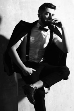 Sakallı adamın elinde matara, stüdyo duvarında ciddi bir yüz var.