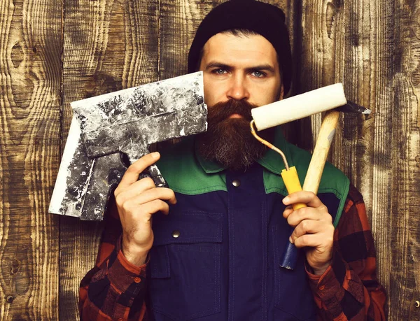 Homem construtor barbudo segurando várias ferramentas de construção com rosto sério — Fotografia de Stock