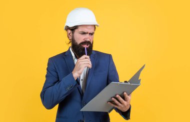Assistant. male builder wearing formal suit and helmet for protection. working on construction project. concentrated man with beard wear hard hat. concept of engineering. architecture and building
