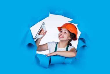 Gerçek mutluluk. Koruyucu şapkalı genç işçi. Kendine güvenen çocuk spatulayı tamir ederken kullanır. İnşaat ve yenileme konsepti. Mutlu kız spatula aleti kullanır. Genç müteahhit güvenlik kaskı takıyor