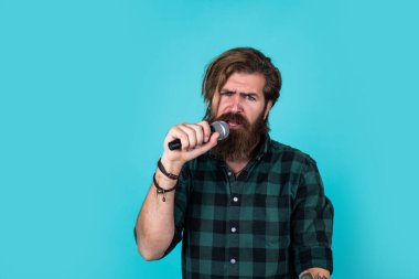 Seminerime gel. Sahnede özgüven ve karizma. Kareli gömlek giyen sakallı bir adam. Rock müzik. Erkek karaoke şarkıcısı. Olgun karizmatik erkek vokalist. Mikrofonda şarkı söyleyen sakallı adam.