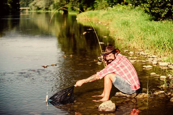 fly fish hobby of man. Hipster in checkered shirt. hipster fishing with spoon-bait. big game fishing. relax on nature. success fisherman in lake water. mature bearded man with fish. Just look at that