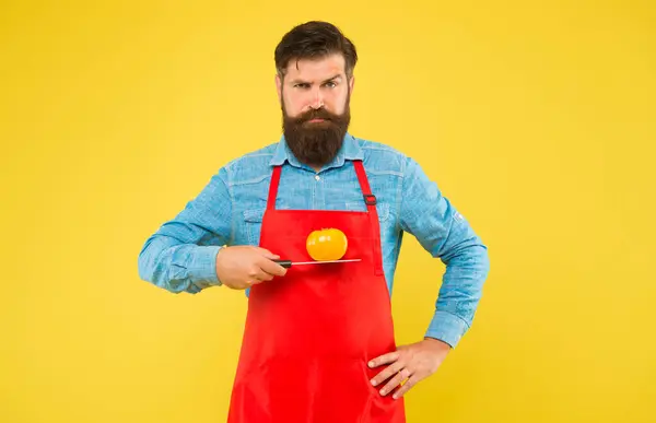 Σοβαρή hipster στην ποδιά μάγειρας κρατήστε ώριμη ντομάτα σε αιχμηρό μαχαίρι κίτρινο φόντο, σνακ — Φωτογραφία Αρχείου