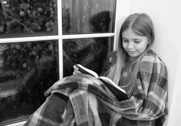 Magic xmas spirit. Little girl enjoy reading Christmas story. Little reader wrapped in plaid sit on window sill. Little child read book on Christmas eve. My favorite Christmas book — Stock Photo, Image