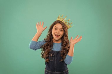 Eğlence uzmanıyım. Çocuk prensesin altın taç sembolünü takıyor. Tatlı kız mavi arka planda dururken taç takıyor. Prenses konsepti ol. Prenses olmayı hayal eden her kız. Küçük hanım prenses.