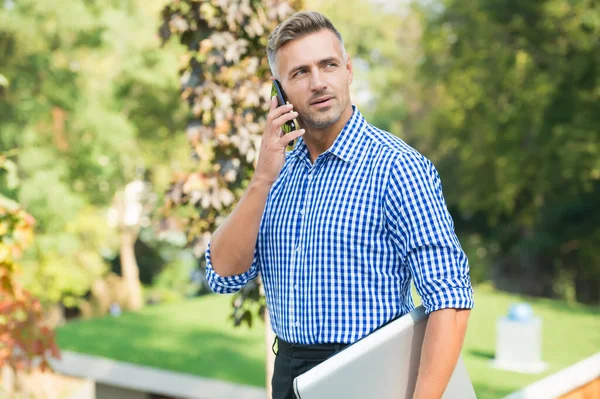 El día comienza con la charla. chico guapo llevar portátil. macho tiene conversación. comunicación en la vida moderna. negocios ágiles. camisa de hombre madura sin afeitar. hombre hablando en el teléfono móvil al aire libre — Foto de Stock